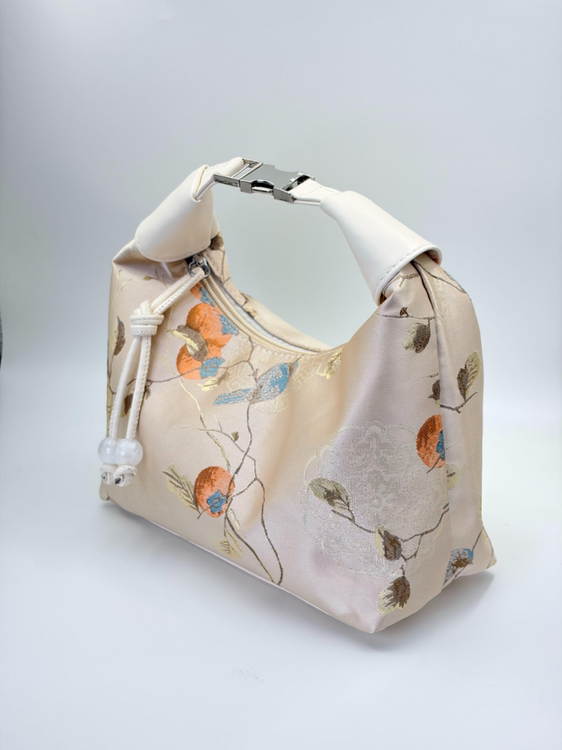 Ivory floral jacquard cosmetic bag with a leather handle and a metal clasp